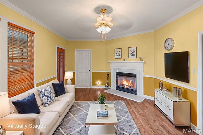 Living area with a glass covered fireplace, ceiling fan, wood finished floors, and crown molding | Image 16