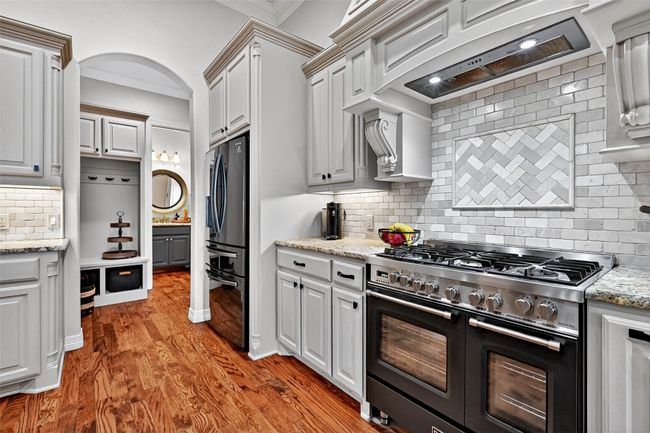 Kitchen featuring stainless steel appliances, tasteful backsplash, crown molding, custom range hood, and light wood finished floors | Image 16