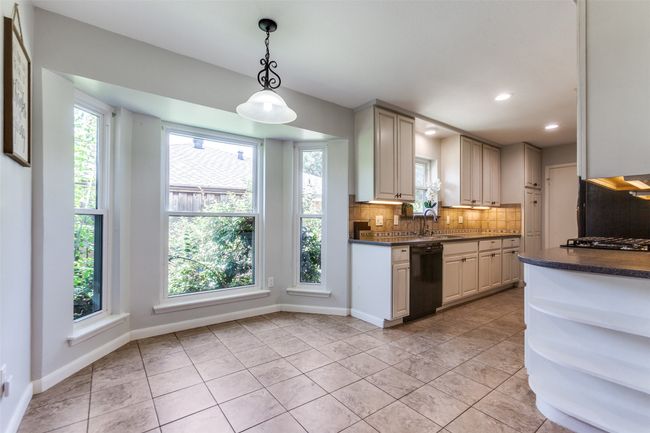 Kitchen featuring black dishwasher, dark countertops, decorative backsplash, pendant lighting, and gas cooktop | Image 7