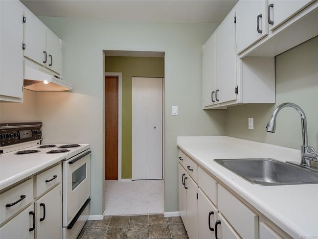 Kitchen with white range with electric stovetop, under cabinet range hood, light countertops, and white cabinetry | Image 8