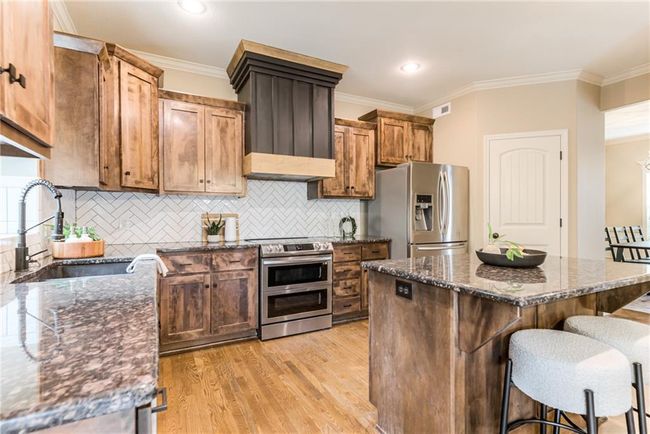 Kitchen featuring stainless steel appliances, crown molding, a breakfast bar area, light wood-type flooring, and dark stone counters | Image 9