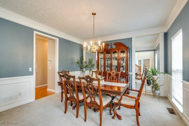 Dining space featuring a chandelier, ornamental molding, light colored carpet, and a wainscoted wall | Image 12