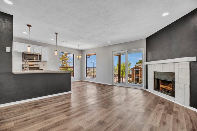 Unfurnished living room featuring a tile fireplace, wood-type flooring, a textured ceiling, and a chandelier | Image 4