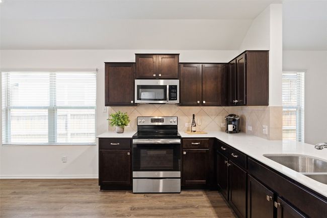 Kitchen featuring appliances with stainless steel finishes, light wood-style flooring, backsplash, dark brown cabinets, and light countertops | Image 12