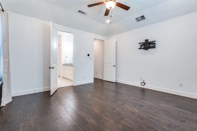 Step into the inviting master bedroom, featuring rich dark wood flooring, a sleek ceiling fan, elegant baseboards, and soft recessed lighting for a warm and relaxing ambiance. | Image 16