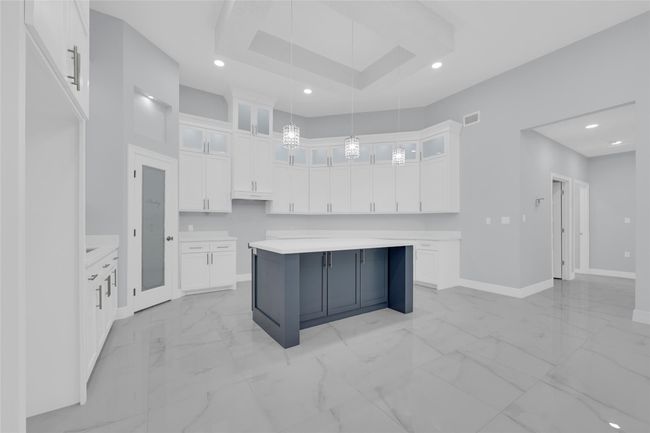 This modern kitchen features sleek white cabinetry, a contrasting dark blue island, and elegant pendant lighting. It's complemented by a spacious layout and light gray walls, creating a bright and inviting space ideal for cooking and entertaining. | Image 12
