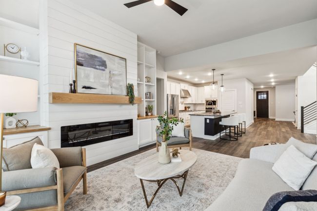 Living room with a ceiling fan, baseboards, dark wood-style flooring, a glass covered fireplace, and stairway | Image 7