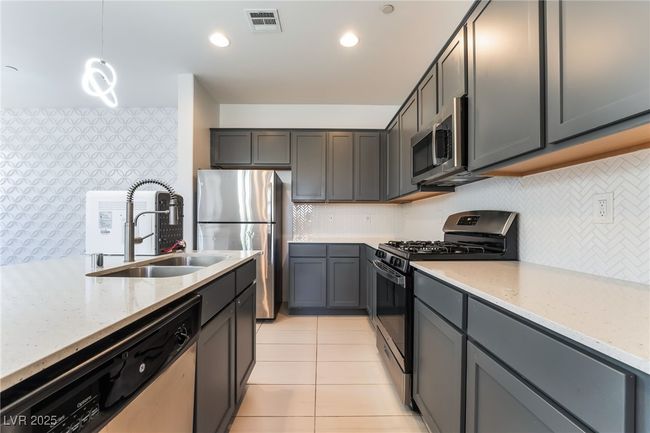 Kitchen with appliances with stainless steel finishes, light stone counters, light tile patterned floors, tasteful backsplash, and hanging light fixtures | Image 16