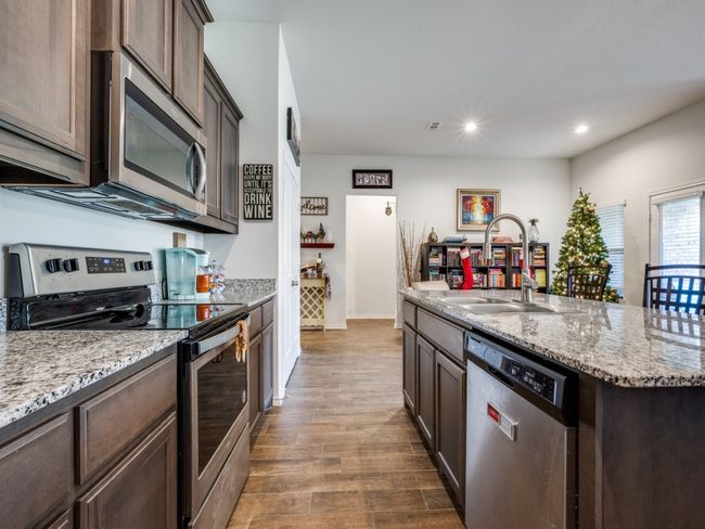 Kitchen featuring stainless steel appliances, dark brown cabinetry, wood finished floors, recessed lighting, and a kitchen island with sink | Image 7