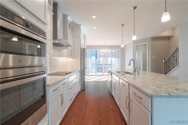 Kitchen featuring stainless steel appliances, hanging light fixtures, backsplash, and wall chimney exhaust hood | Image 5