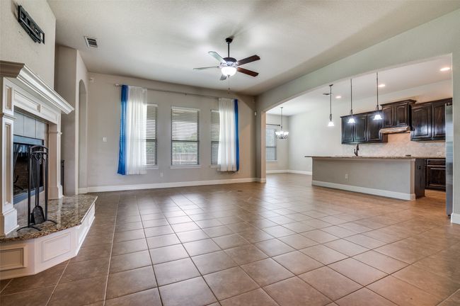 Unfurnished living room featuring arched walkways, a fireplace, tile patterned flooring, a ceiling fan, and a chandelier | Image 4
