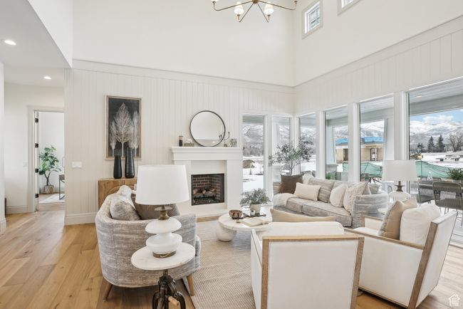 Living room featuring light wood-type flooring, a notable chandelier, a fireplace, and a towering ceiling | Image 4