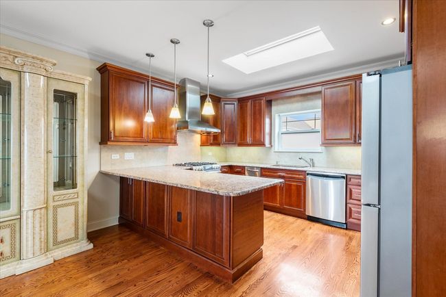 Kitchen with a peninsula, a skylight, appliances with stainless steel finishes, wall chimney exhaust hood, and light wood finished floors | Image 5