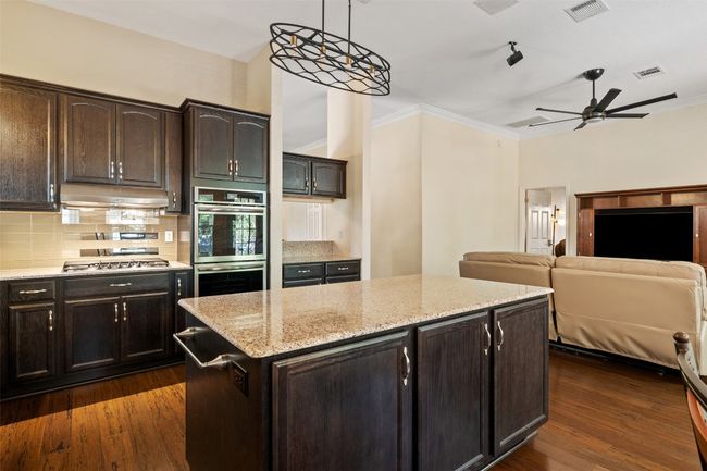 Kitchen with appliances with stainless steel finishes, under cabinet range hood, decorative backsplash, a ceiling fan, and a center island | Image 16