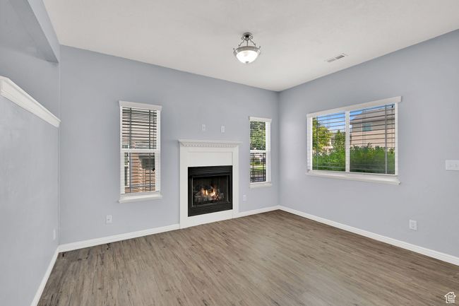 Unfurnished living room featuring wood finished floors and a lit fireplace | Image 12