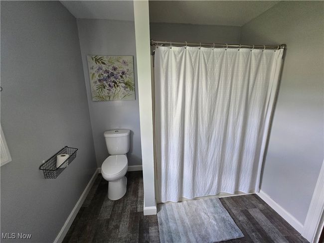 Bathroom featuring baseboards, wood finished floors, curtained shower, and toilet | Image 11