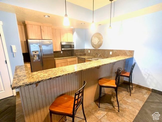 Kitchen featuring appliances with stainless steel finishes, light brown cabinets, a peninsula, decorative backsplash, and light stone counters | Image 5