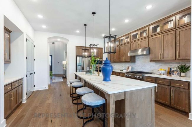 Kitchen with under cabinet range hood, stainless steel appliances, arched walkways, decorative backsplash, and a breakfast bar area | Image 5