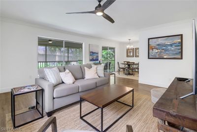 Living room with ornamental molding, light hardwood / wood-style flooring, and ceiling fan with notable chandelier | Image 1