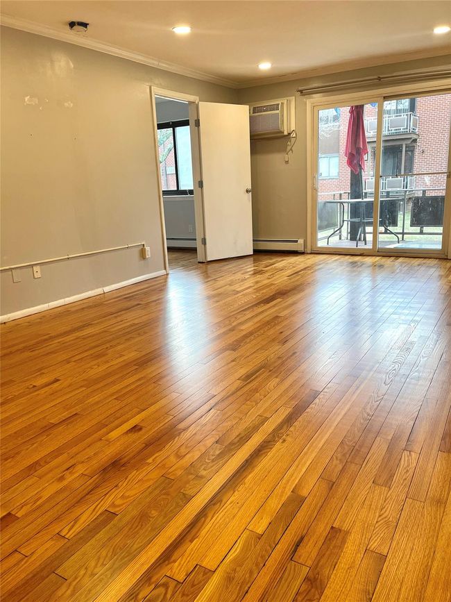 Empty room with a baseboard heating unit, wood finished floors, an AC wall unit, and ornamental molding | Image 7