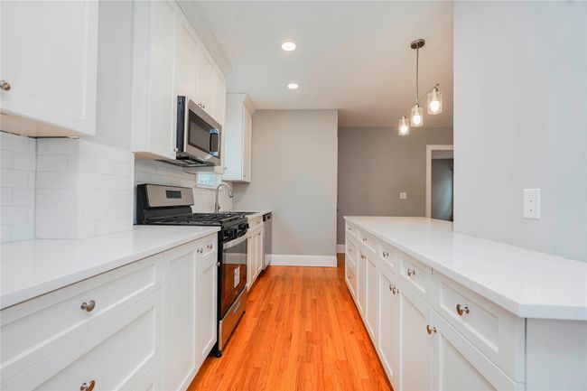 Kitchen with tasteful backsplash, light wood-type flooring, light countertops, white cabinetry, and stainless steel appliances | Image 16