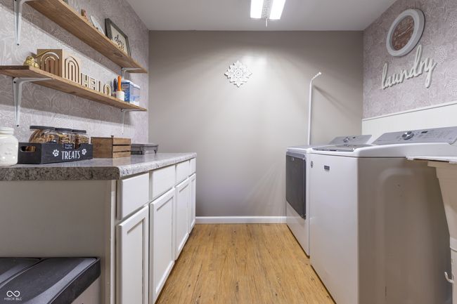 laundry area featuring washing machine and clothes dryer, light wood-style flooring, and cabinet space | Image 30