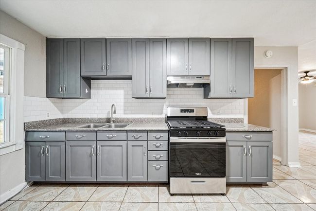 Kitchen with stainless steel gas range oven, under cabinet range hood, gray cabinetry, tasteful backsplash, and healthy amount of natural light | Image 10