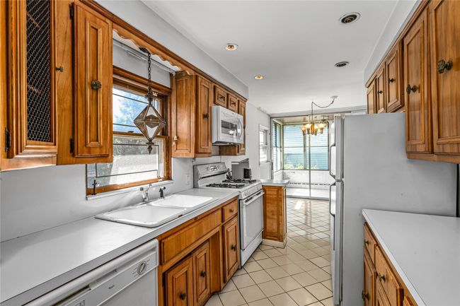 Kitchen featuring light tile patterned flooring, a chandelier, white appliances, brown cabinets, and a sink | Image 5