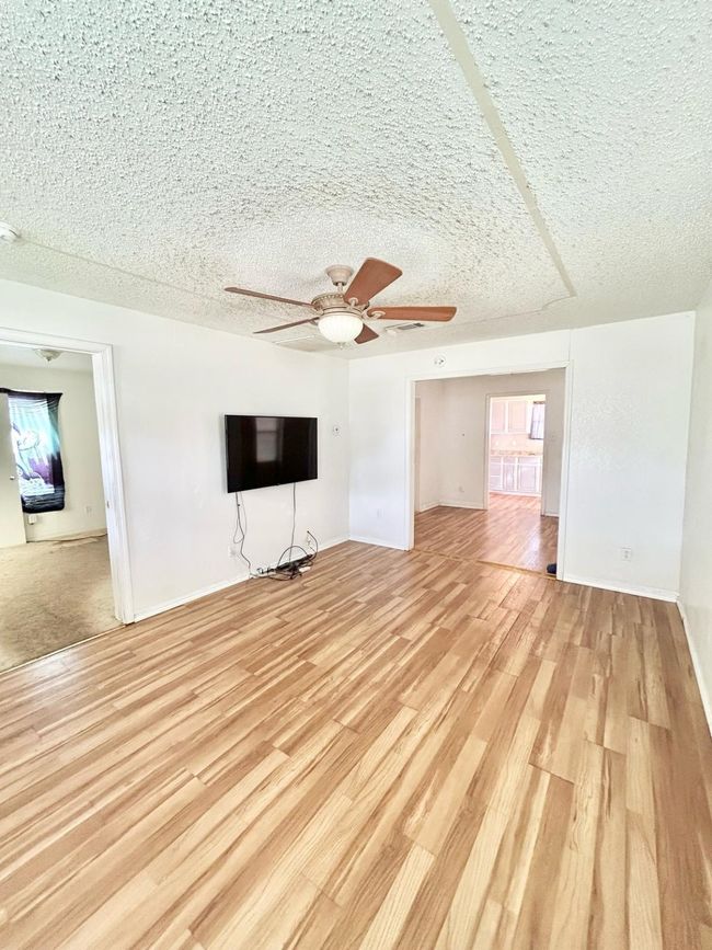 Unfurnished living room featuring ceiling fan, light wood finished floors, baseboards, and a textured ceiling | Image 10