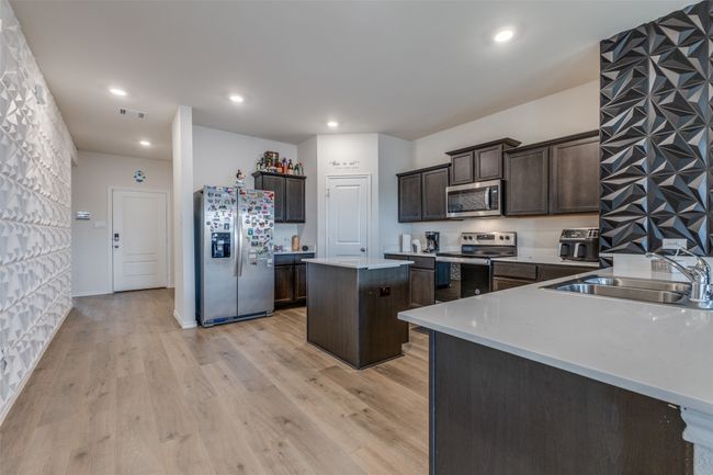 Kitchen with stainless steel appliances, a kitchen island, a sink, light wood-style floors, and dark brown cabinetry | Image 4