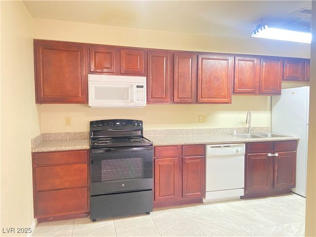 Kitchen with white appliances, light tile patterned floors, a sink, light countertops, and dark brown cabinets | Image 8