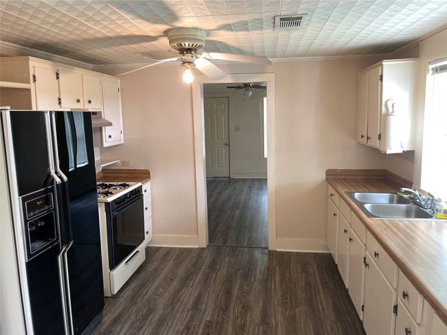 Kitchen featuring black fridge, range with gas stovetop, a sink, range hood, and baseboards | Image 9