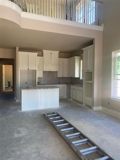 Kitchen with backsplash, stone countertops, white cabinetry, a kitchen island, and a towering ceiling | Image 2