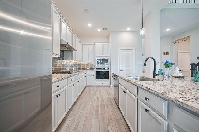 Chef’s dream kitchen features granite countertops, custom backsplash, white cabinetry, a gas cooktop, built-in double ovens, and a walk-in pantry. | Image 12