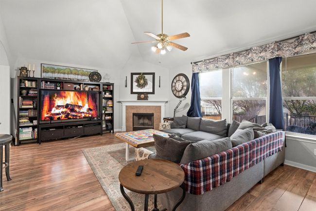 Living area with a ceiling fan, vaulted ceiling, a fireplace, and wood finished floors | Image 4