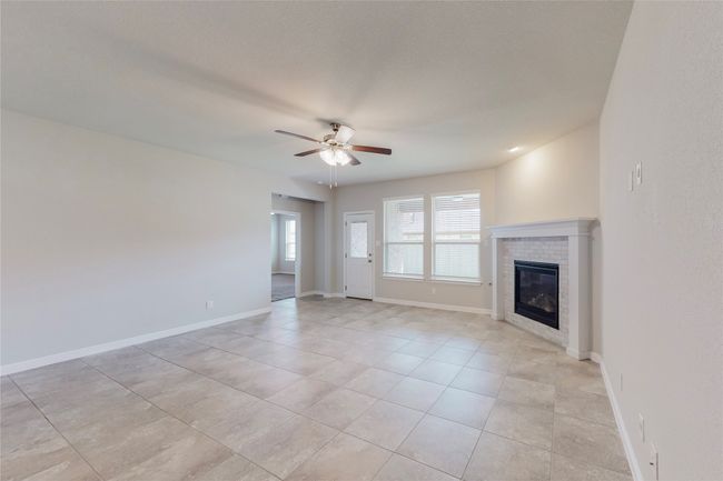 Unfurnished living room with a ceiling fan, a brick fireplace, light tile patterned flooring, and baseboards | Image 12