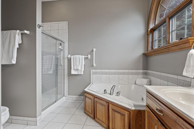 Private primary bath offers a separate tiled shower and grab bars (which easily could be removed if you prefer). White tile and a beautiful arched window creates that pristine spa like ambiance. | Image 20