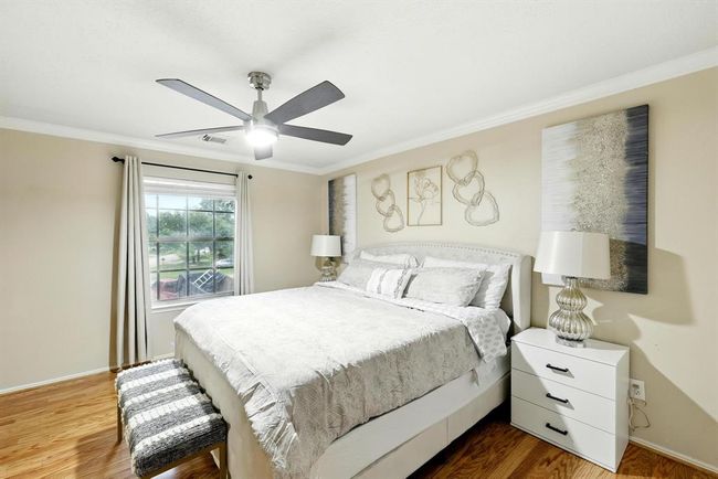 Serene primary suite with wood flooring, crown molding, a modern ceiling fan, and large window offering natural light and neighborhood views. | Image 14