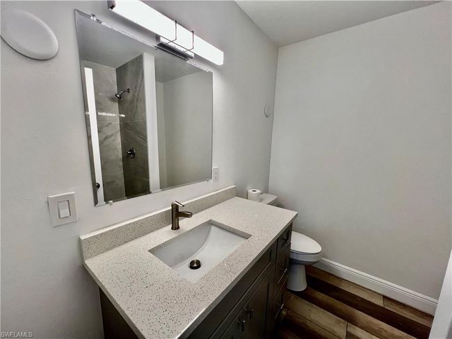 Full bathroom with toilet, a tile shower, baseboards, wood finished floors, and vanity | Image 24