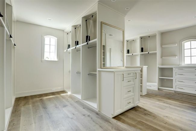 The expansive primary closet is a dream for any fashion enthusiast. Designed in a boutique style, it features abundant cabinetry and custom-built shelves for shoes and accessories. A spacious wall of hanging storage elegantly divides the room into two distinct closet spaces, offering both functionality and sophistication. | Image 18