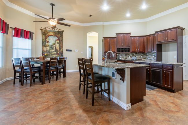 Kitchen with arched walkways, a ceiling fan, ornamental molding, tasteful backsplash, and light stone counters | Image 7