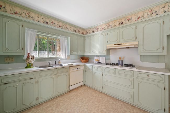 Kitchen with under cabinet range hood, white appliances, light flooring, light countertops, and green cabinetry | Image 12