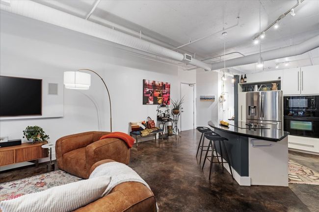 Kitchen with black appliances, finished concrete floors, a breakfast bar, white cabinets, and dark countertops | Image 14