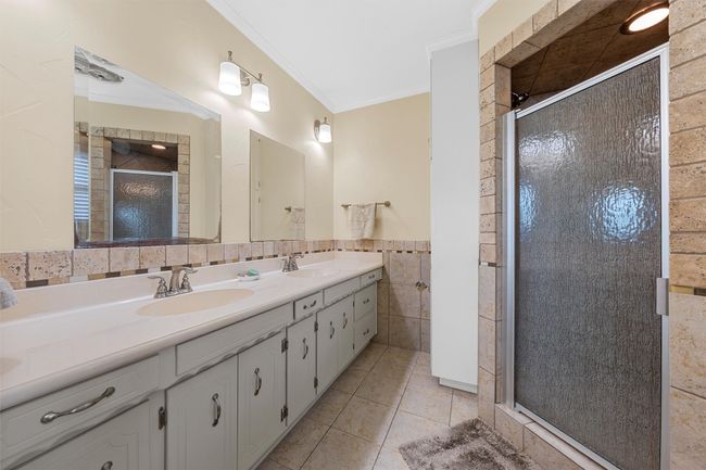 Bathroom featuring double vanity, tile walls, a stall shower, tile patterned flooring, and ornamental molding | Image 18