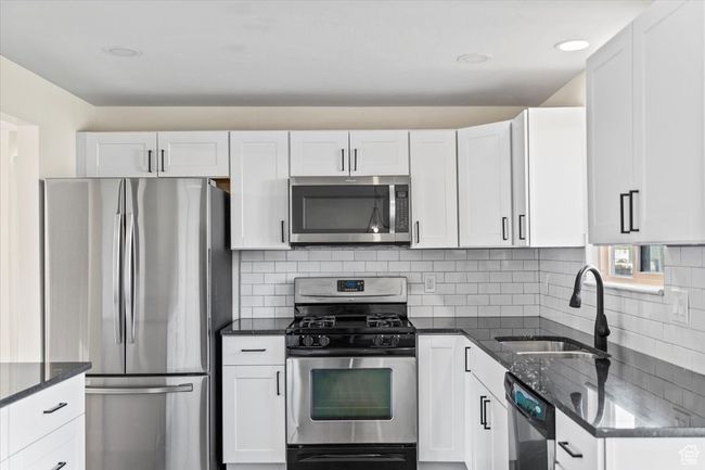 Kitchen with dark stone counters, a sink, stainless steel appliances, and white cabinetry | Image 11