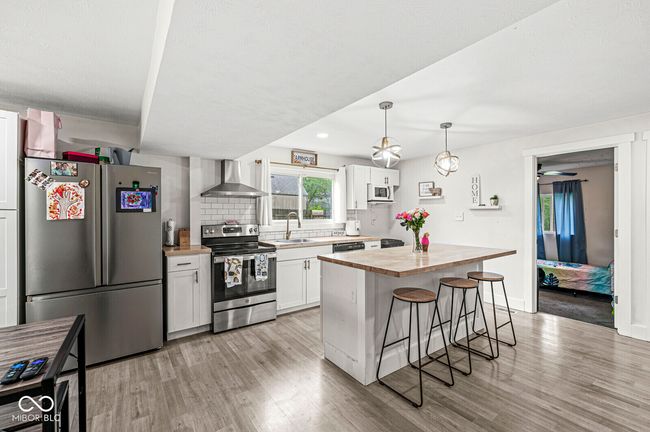 kitchen featuring stainless steel appliances, wall chimney range hood, butcher block counters, a breakfast bar, and light wood-type flooring | Image 9