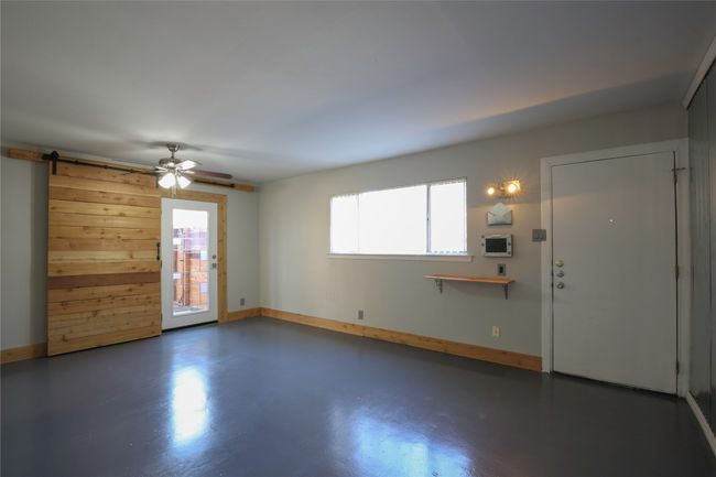 Unfurnished living room with ceiling fan, wood walls, and concrete floors | Image 5