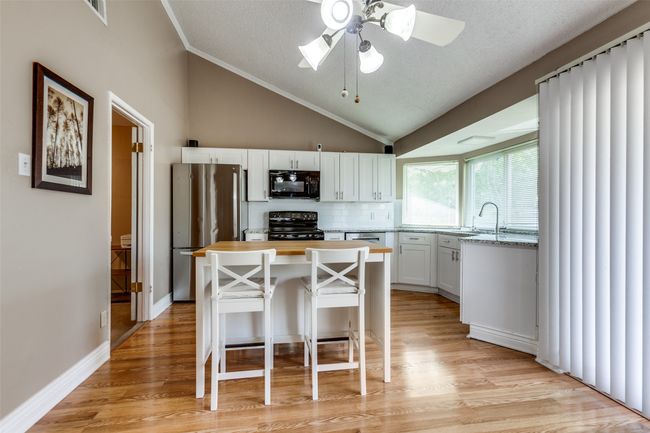 Kitchen featuring black appliances, vaulted ceiling, a ceiling fan, a kitchen island, and white cabinets | Image 4