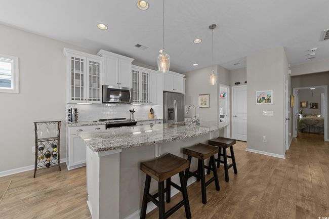 Kitchen featuring stainless steel appliances, tasteful backsplash, a center island with sink, light wood-style flooring, and baseboards | Image 6