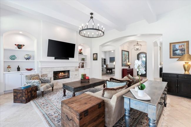 Living room with arched walkways, built in features, beamed ceiling, a chandelier, and a fireplace | Image 4